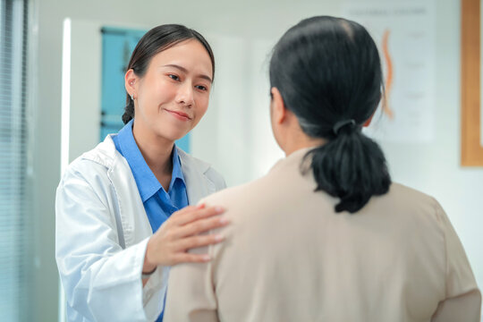 Happy Asian female doctor demonstrates compassionate care, holding hands with senior patient. Therapeutic touch approach showcases empathetic healthcare delivery and patient-centered emotional support