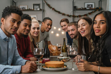 Group of Friends and Family Enjoying Festive Thanksgiving Dinner Indoor Holiday Table with Roasted Turkey, Cheesecake, and Red Wine Warm Celebration with Smiles, Garland Accents, and Framed Photos