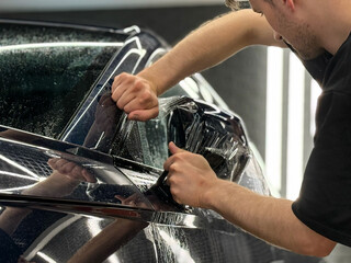 A car wrapping specialist applies a polyurethane film to the car. Detailer smoothes PPF. Car wrapping, detailing, tuning and styling. PPF protective film against chips and scratches. Car protection.