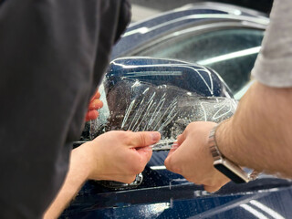 A car wrapping specialist applies a polyurethane film to the car. Detailer smoothes PPF. Car wrapping, detailing, tuning and styling. PPF protective film against chips and scratches. Car protection.