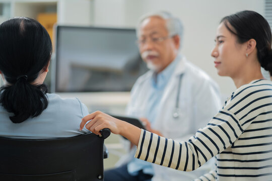 Asian daughter accompanies senior mother for medical consultation with doctor using digital health technology. Family centered care demonstrates intergenerational support and patient advocacy through