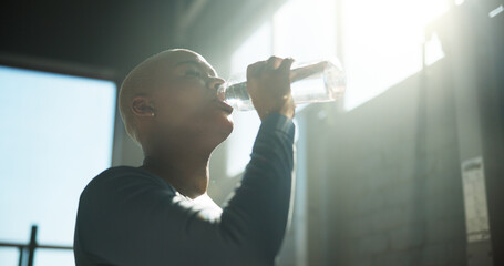 Woman, fitness and drinking with water bottle for hydration, recovery or break in gym. Active, female person or thirst with natural mineral liquid for rest, performance or energy in health club