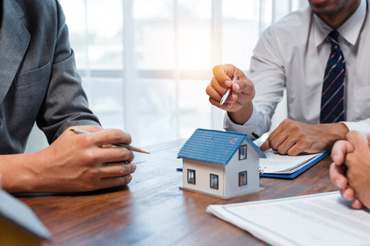 Real estate agent pointing at a house model while discussing a contract with potential clients during a meeting
