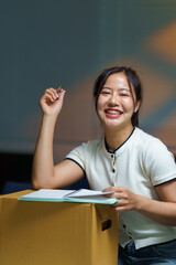 Naklejka premium Happy young Asian woman taking notes while using a cardboard box as a makeshift desk during a home or office move