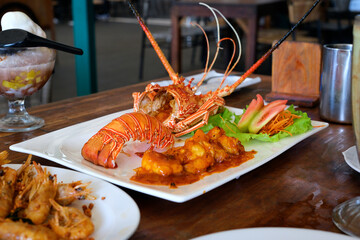 Freshly cooked lobster served with savory sauce and vegetables on a white plate, captured in a restaurant setting with natural lighting and a slightly angled perspective.