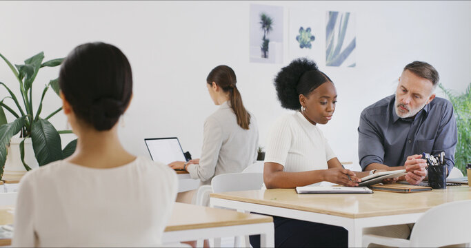 Tablet, business people and discussion in meeting to review brand proposal with mentor. Technology, planning and creative team in office for logo, help and training with graphic design intern