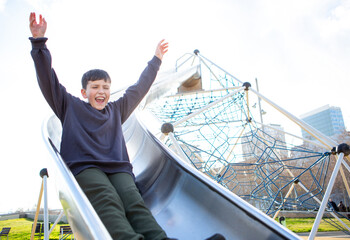 Excited boy riding down a tall metal slide with arms raised high