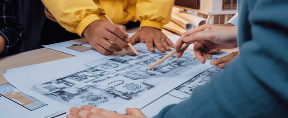 A group of professionals engage in a creative meeting, closely analyzing detailed architectural floor plans and sketches on a collaborative workspace table. SACTR