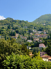 A picturesque hillside town in Italy, with charming houses and cypress trees nestled among lush green slopes under a clear blue sky.