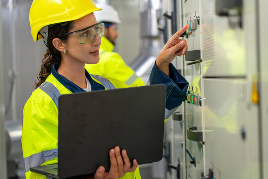 Female electrician inspects HVAC, pipelines, and machinery inside factory using digital tools for safety and operational connecti