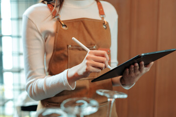 Close up of a waitress taking orders in a restaurant while using a digital tablet and stylus pen, showcasing modern hospitality technology