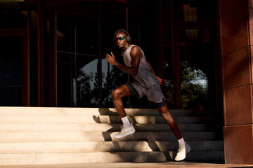 Fototapeta premium Athletic man running outdoors wearing headphones and sunglasses on urban stairs
