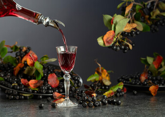 Black chokeberry liqueur and fresh berries on a black stone table.