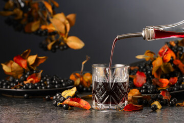 Black chokeberry juice and fresh berries on a black background.