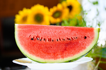 室内のテーブルに置かれた切ったスイカと風に揺れるひまわりの花