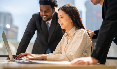 Diverse group of business professionals in formal collaborating during a corporate meeting, focused on technology and teamwork, asian businesswoman leading with laptop, teamwork and collaboration