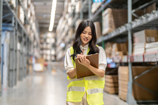 Asian warehouse staff woman checking inventory with clipboard in logistics management, working in supply chain, e-commerce, shipping, warehouse management and distribution center industry business