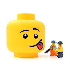 Naklejka premium Lego minifigures are showing at the large yellow head with funny face is sticking out the tongue isolated on white. Editorial illustrative image of popular plastic toy.