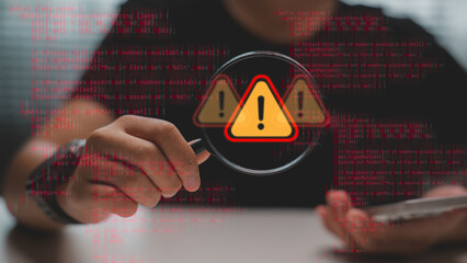 Magnifying glass focusing on warning error sign with programming code background. Concept of cyber security, data protection, system bug, hacker threat, and technology risk detection.
