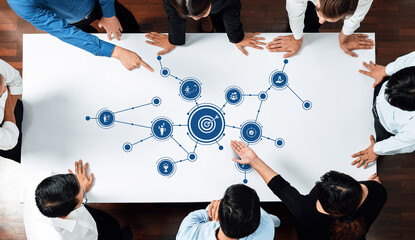 A diverse business team engages in a collaborative discussion over a strategy table, focusing on targets and innovative goals through visual icons in a modern office. Amity