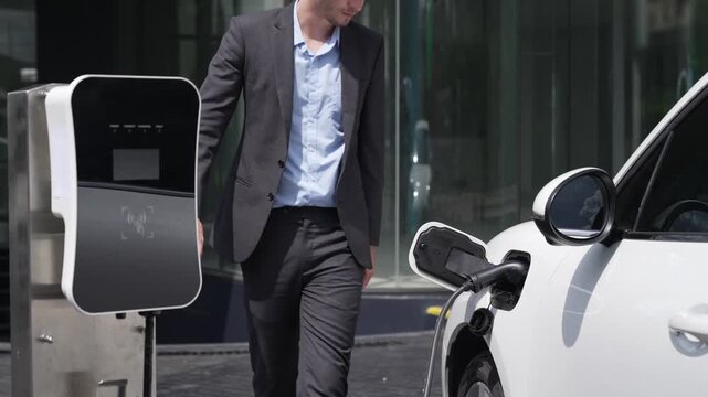 Progressive businessman unplugs charger plug from charging station to his electric car before driving around city center. Eco friendly rechargeable car powered by sustainable and clean energy.