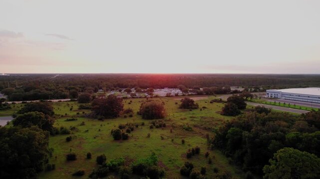 Drone aerial view of Ocala, Florida landscape with fields, trees, and warehouses at sunset, symbolizing growth and development.