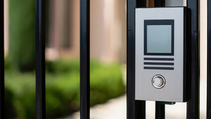 Closeup of a modern intercom system on a black metal gate with greenery