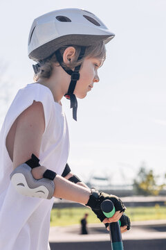 Child in safety helmet and elbow pads rides scooter outdoors
