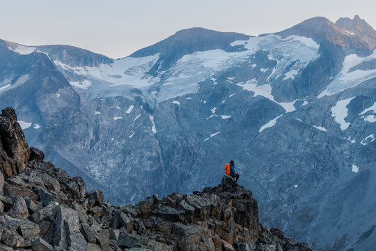 female backpacker standing on the edge of a cliff looking at glacier