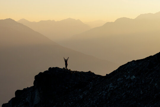 Hiker standing on summit, reaching for the sky, success.