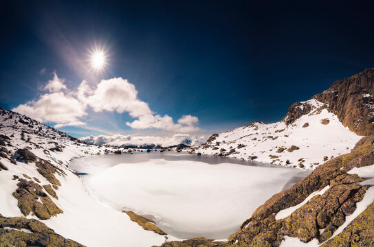 Frozen glacial lake surrounded by snow-capped mountains and illu