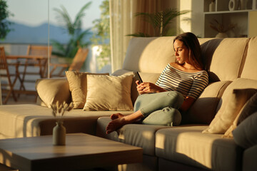 Obraz premium Woman at sunset using mobile phone on a sofa