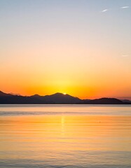 Fototapeta premium Serene Sunset Over Calm Water and Mountains.