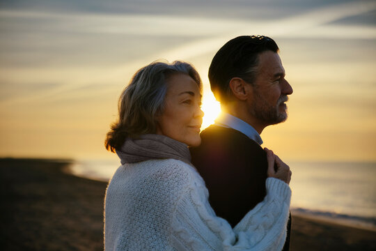 Smiling mature woman and man enjoying sunrise at beach