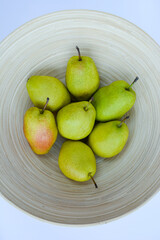 bamboo plate with ripe pears on light background, close-up