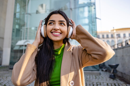 Thoughtful young woman wearing headphones outside building