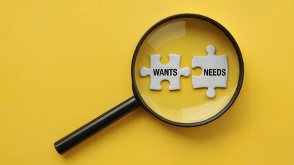 Magnifying glass focusing on Wants and Needs jigsaw puzzle pieces, highlighting business strategy and consumer insights, on yellow