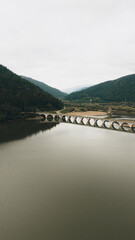 Long bridge reflecting in lake between green mountains
