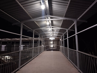 Railway station foot overbridge at night with roof and lights – empty pedestrian walkway over train tracks