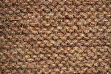 Dark brown wool knitted fabric texture, macro. Close-up view of warm, fuzzy wool yarn in a dense hand-knitted pattern. Natural textile structure with visible fibers and stitches