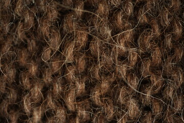 Dark brown wool knitted fabric texture, macro. Close-up view of warm, fuzzy wool yarn in a dense hand-knitted pattern. Natural textile structure with visible fibers and stitches