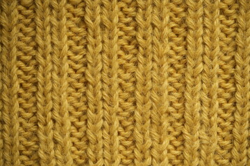 macro texture of yellow knitted wool fabric. The soft and cozy hand-knitted textile features a ribbed pattern with visible yarn loops and detailed stitches. Ideal background for fashion, textile