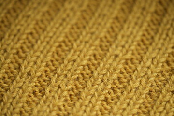 macro texture of yellow knitted wool fabric. The soft and cozy hand-knitted textile features a ribbed pattern with visible yarn loops and detailed stitches. Ideal background for fashion, textile
