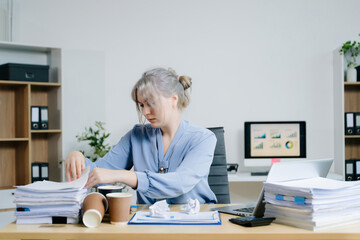 Focused businesswoman sorting documents at a cluttered desk with reports, coffee cups, and files. Perfect for accounting, finance, tax season, and deadline stress concepts.