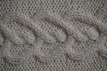 white texture of knitted wool fabric as a background, ivory smooth symmetrical braided cable knit pattern of hand-knitted needlework