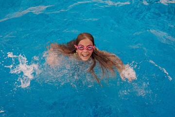 Happy girl wearing googles girl on water in swimming pool. Travel lifestyle into blue water. Summer holiday, girl in see