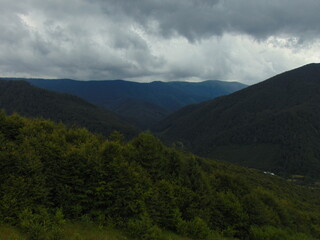 Dark clouds loom over lush green Carpathian mountains, creating a dramatic contrast of light and shadow in the vast, untouched wilderness of the natural landscape