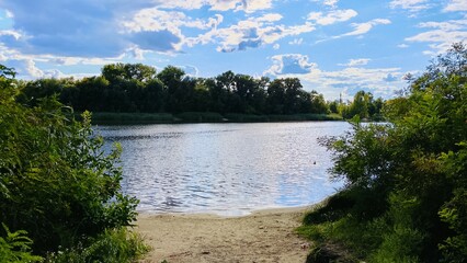 big white clouds over blue river, greenery along the river