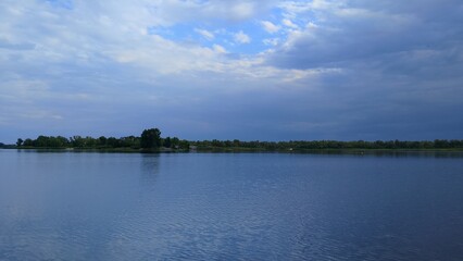 big white clouds over blue river, greenery along the river