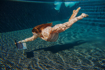 Businesswoman reaching for laptop at bottom of swimming pool